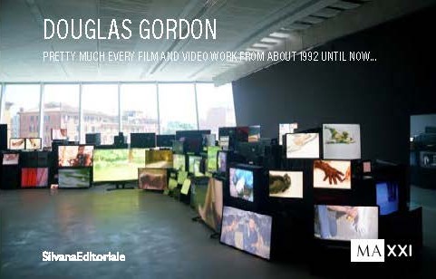 Copertina di catalogo con il titolo “Douglas Gordon – Pretty much every film and video work from about 1992 until now…”. La fotografia mostra un’installazione museale con decine di monitor e televisori di varie dimensioni, impilati e disposti a formare un’onda che attraversa una sala dalle alte finestre, ciascuno con un’immagine video diversa in riproduzione. In basso, i loghi di “Silvana Editoriale” e “MAXXI”.