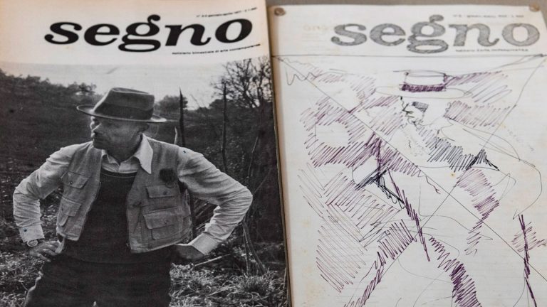 Due copertine affiancate della rivista "segno". A sinistra, una fotografia in bianco e nero di Joseph Beuys con cappello a tesa larga, giacca con molte tasche e mani sui fianchi, ritratto all'aperto tra vegetazione secca. A destra, un'altra copertina della stessa testata, su cui è sovrapposto un disegno a penna nei toni del viola e del nero: la figura schizzata di una persona con cappello, realizzata con tratti rapidi e tratteggi incrociati, in stile gestuale e astratto.